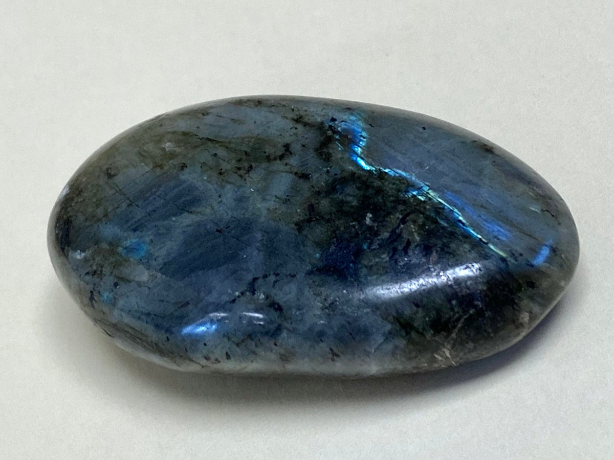 A polished labradorite palm stone, grey-green with a bright flash of blue across its surface.
