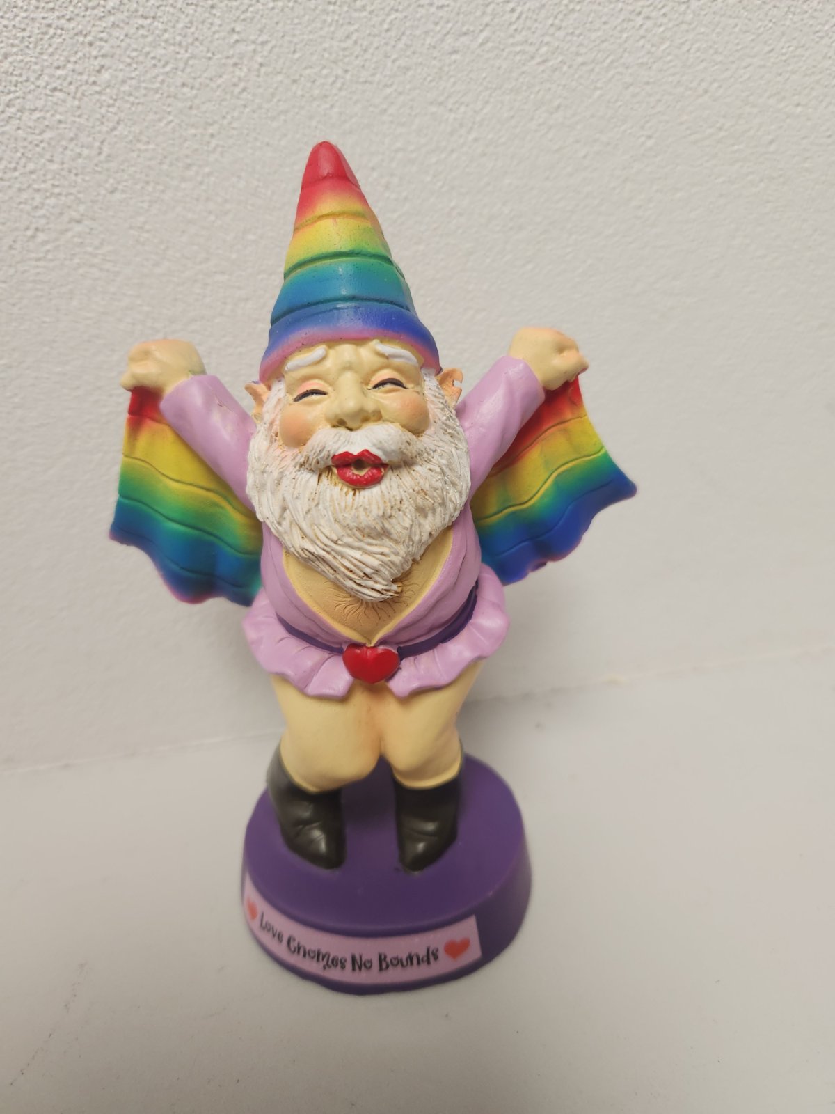 Colorful rainbow gnome figurine with white beard, pink outfit, and rainbow wings on purple base