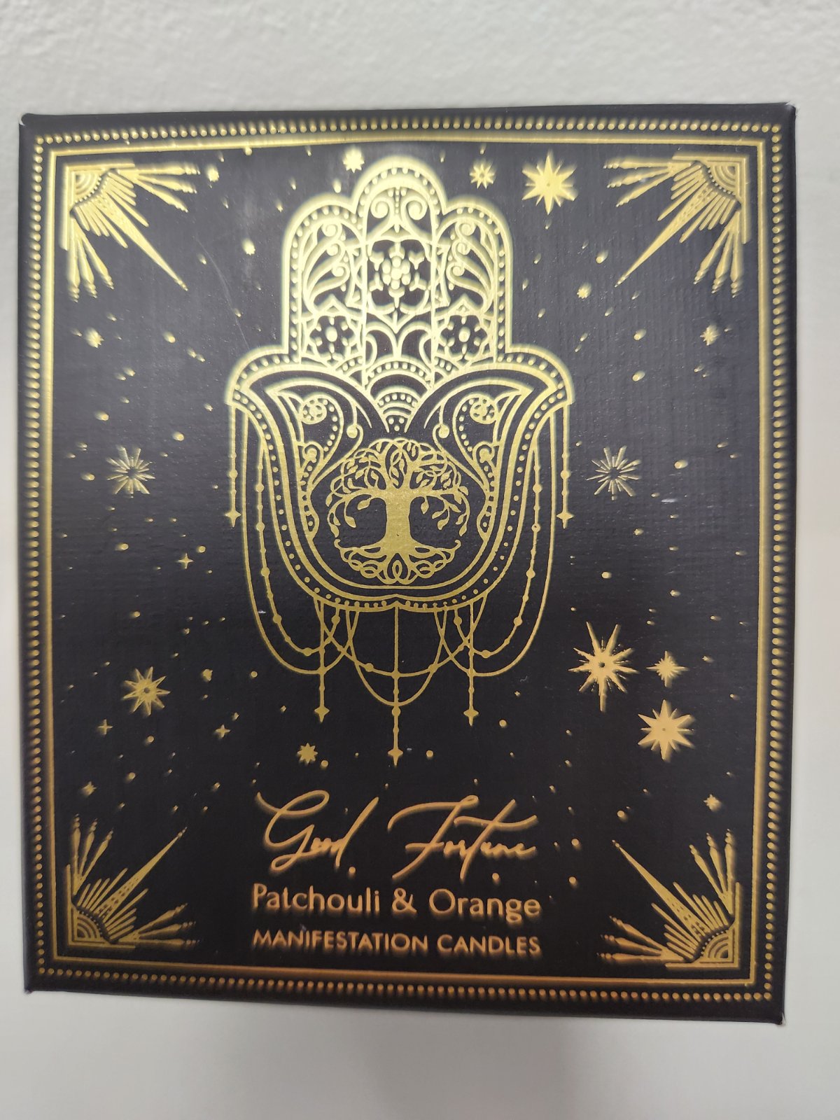Good Fortune Patchouli & Orange Manifestation Candle with ornate gold hamsa hand and tree design on black box