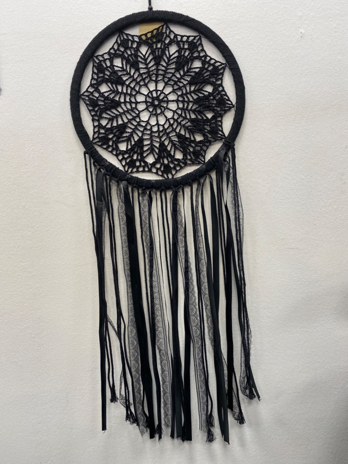 Black crochet dream catcher with intricate webbed mandala pattern and long black fringe strands