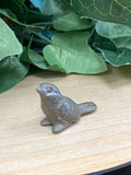 Small pyrite bird carving on wooden surface with green foliage backdrop