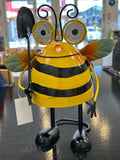 Yellow and black metal bee garden ornament with reflector eyes, shovel, and green wings, indoors