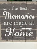 Wooden wall art with white script text reading 'The Best Memories are made at Home' with a key icon, mounted on grey weathered timber planks