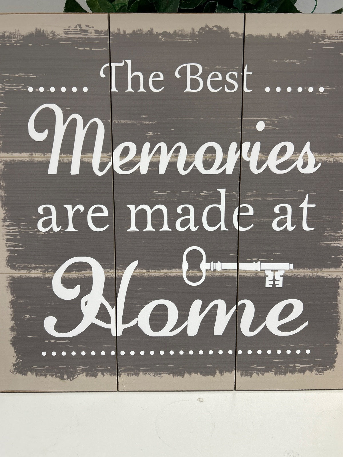Wooden wall art with white script text reading 'The Best Memories are made at Home' with a key icon, mounted on grey weathered timber planks
