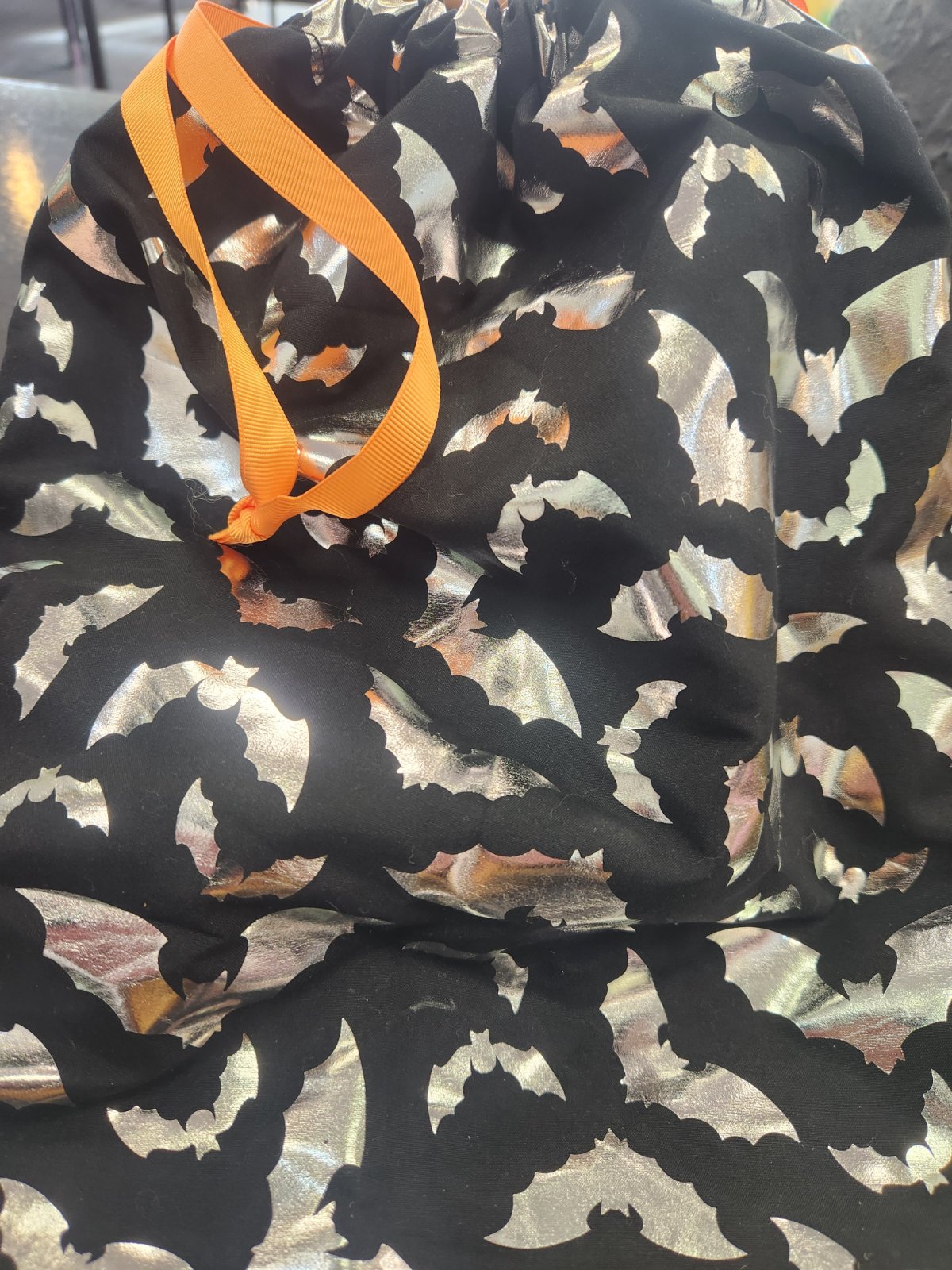 Black drawstring bag with silver bat print pattern and bright orange grosgrain ribbon handle