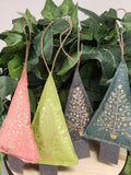 Four fabric Christmas tree ornaments in pink, lime, navy, and teal, each with gold botanical designs and jute hangers, hanging in greenery.
