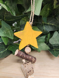 Yellow wooden star ornament hanging from cream rope, displayed against green foliage