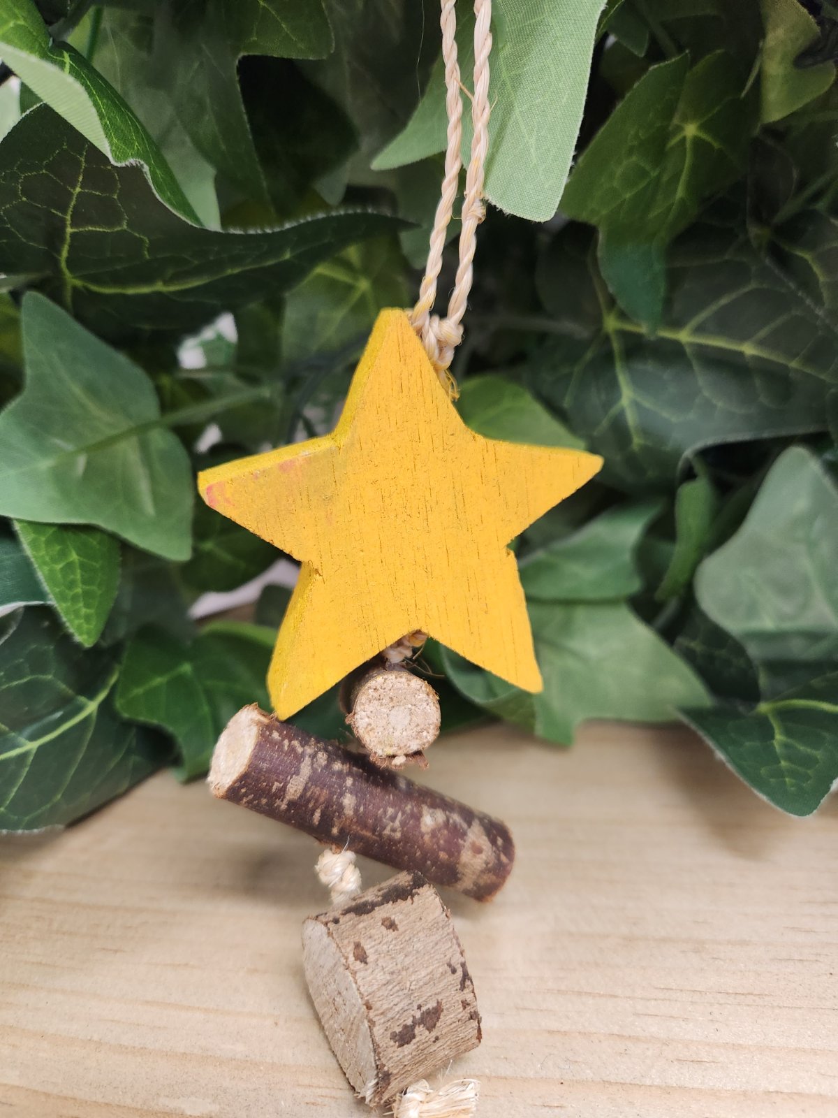 Yellow wooden star ornament hanging from cream rope, displayed against green foliage