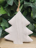 White washed wooden Christmas tree ornament with twine loop, hanging in front of green leaves