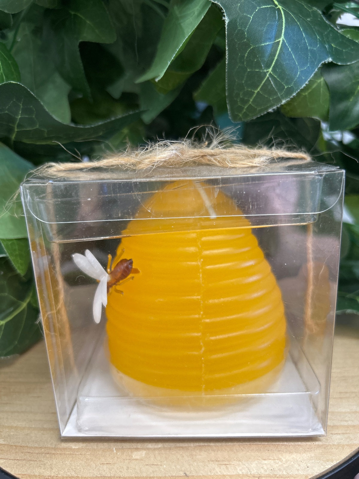 Yellow beeswax hive-shaped candle in clear box with straw lid and a bee visitor on white flowers