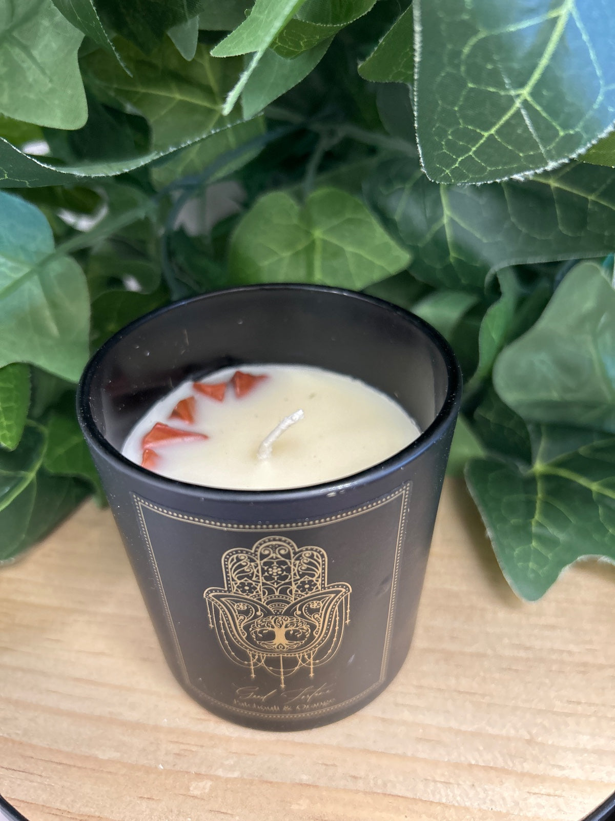 Black Good Fortune Manifestation Candle with gold hamsa hand design, cream wax and dried orange petals visible inside.