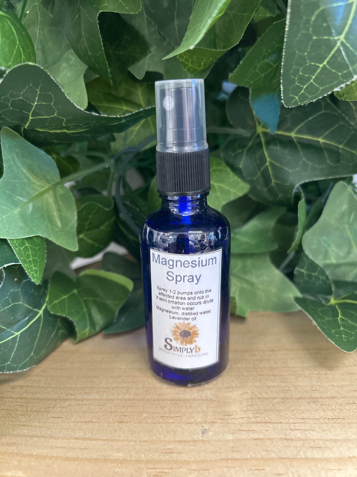 Blue glass spray bottle of Magnesium and Lavender Spray with black pump top, surrounded by green leafy plants.