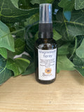 Dark glass spray bottle of Magnesium and Rose Spray by SimplyB, with white label and black pump top, surrounded by green leaves