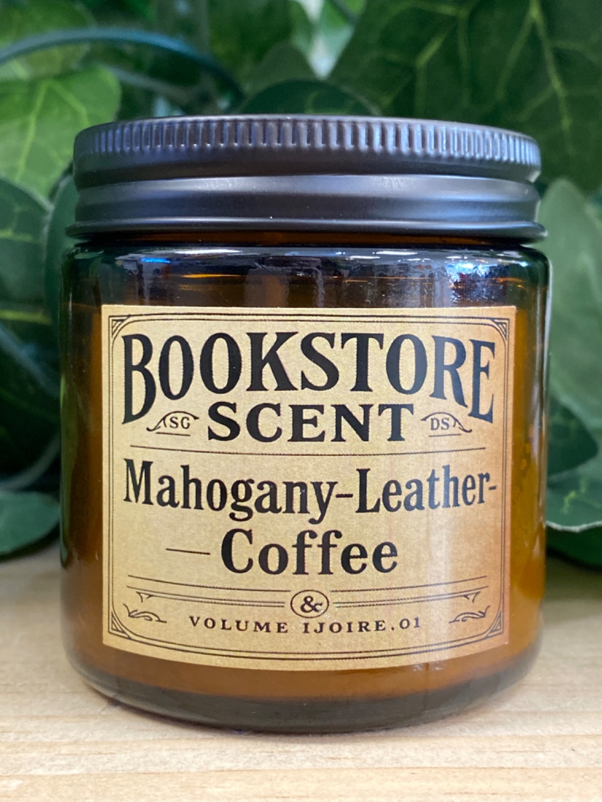 Bookstore Scent candle in amber glass jar with black metal lid and cream label reading Mahogany-Leather-Coffee
