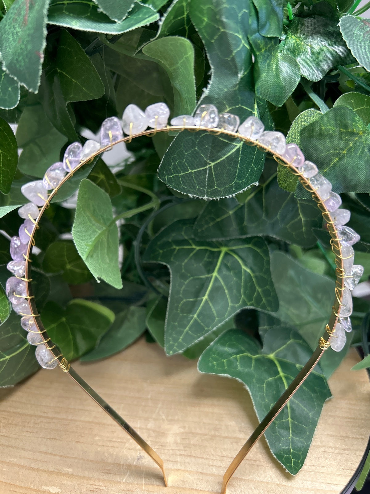 Amethyst crystal headband with pale purple beads on gold wire, displayed in green foliage