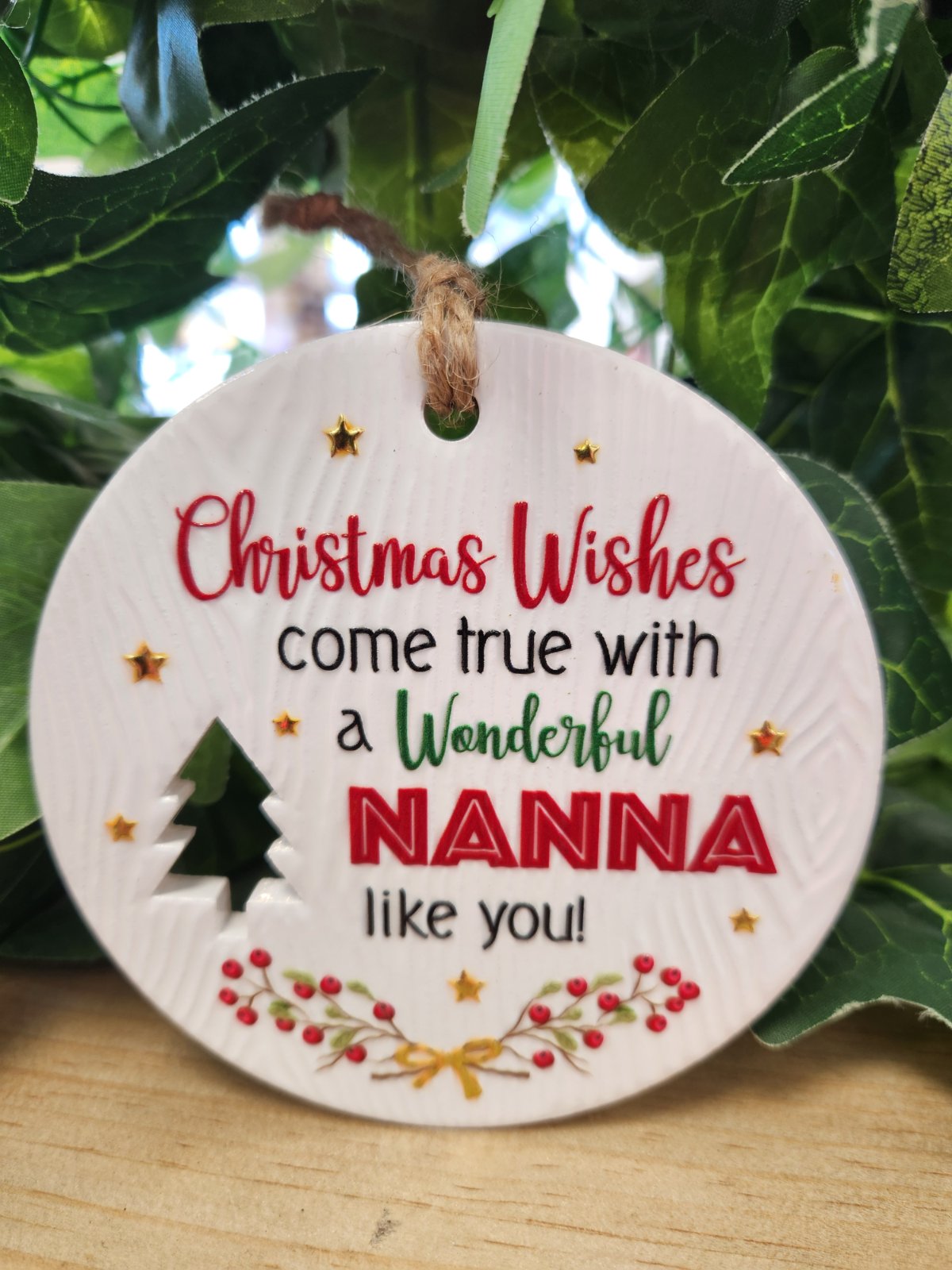 White ceramic round Christmas ornament with red and gold text reading 'Christmas Wishes come true with a Wonderful NANNA like you' decorated with gold stars, a green tree, and red berries