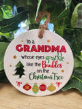 Round ceramic Christmas ornament for grandma with red and green text, tree and bauble designs, twine loop