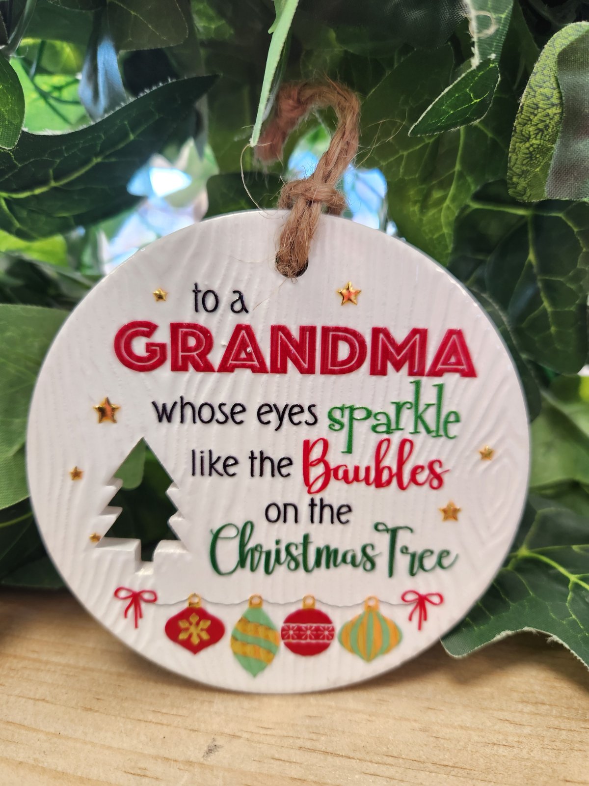Round ceramic Christmas ornament for grandma with red and green text, tree and bauble designs, twine loop