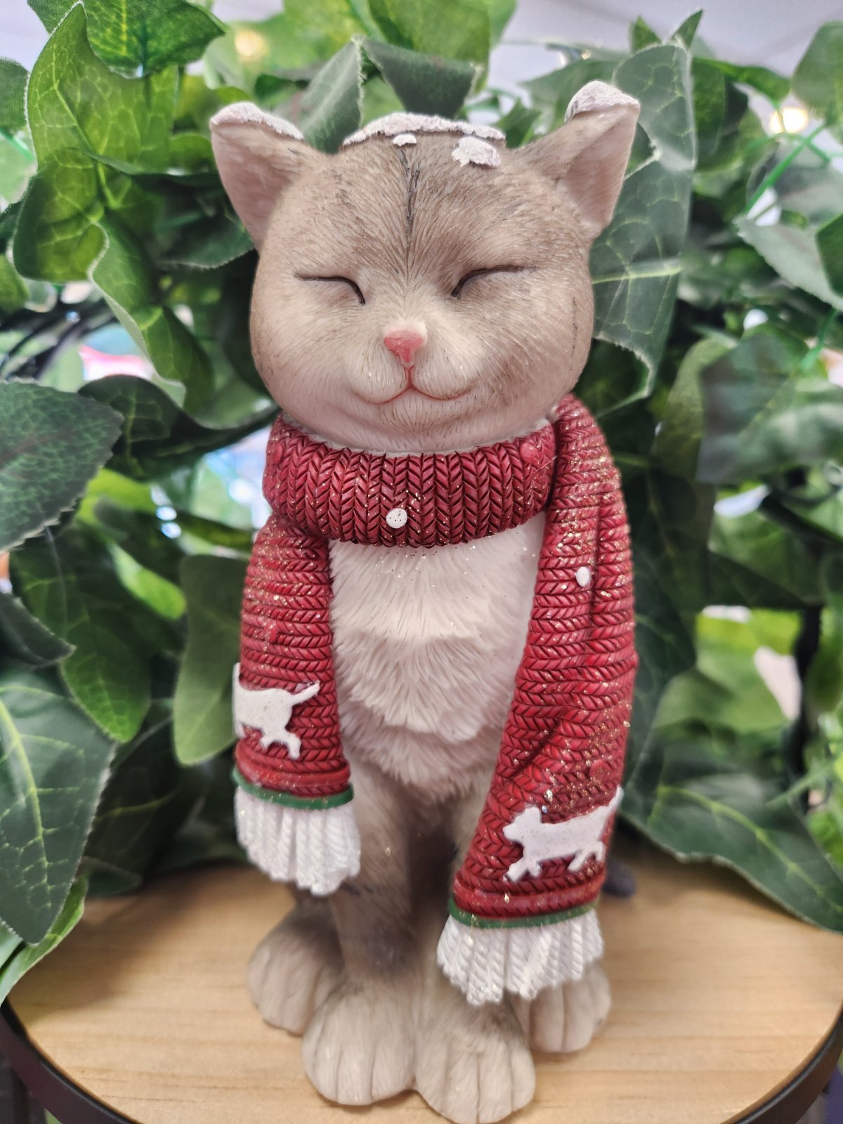 Grey and white ceramic cat figurine wearing a red knitted scarf with white trim and small cat motifs