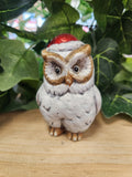 Small ceramic Christmas owl figurine wearing a red and white Santa hat, white body with brown markings, sitting on wood.