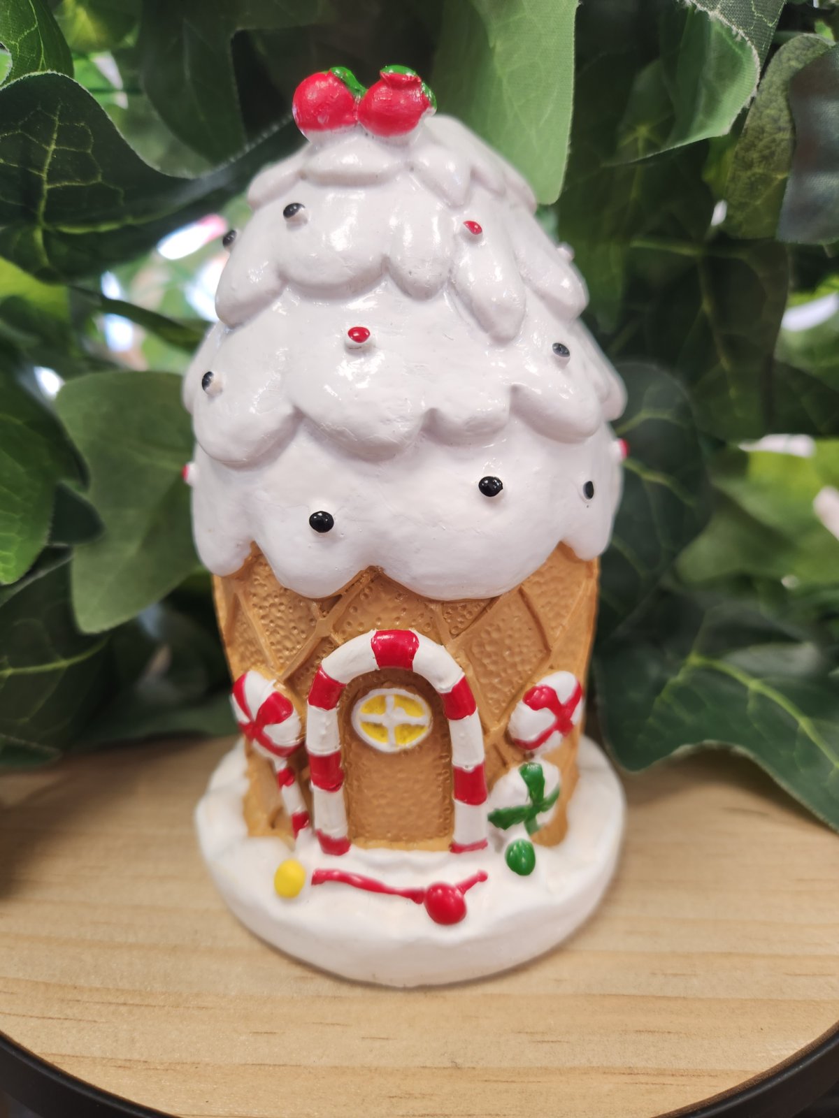 Ceramic gingerbread house candle holder with white icing roof, candy cane door, and red berries on top.