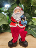 Hand-painted Santa figurine with white beard and red suit, holding a small blue bird, mounted on black boots with swinging legs