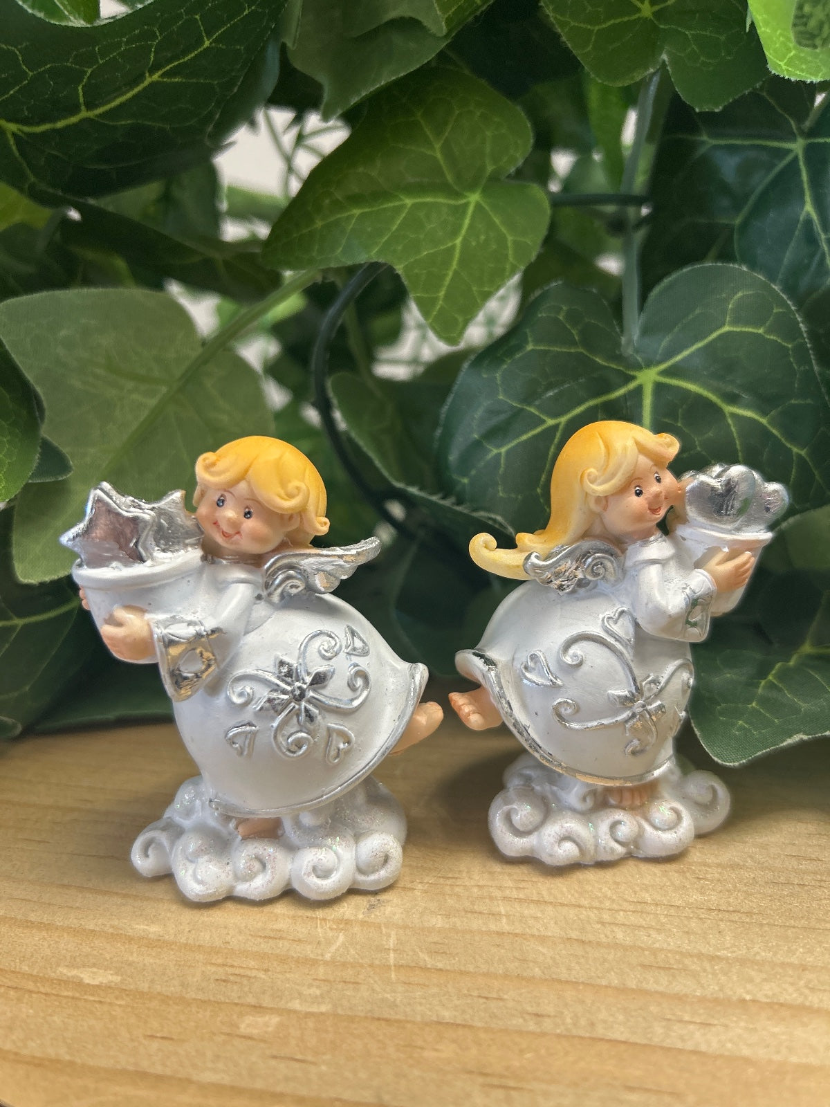 Two ceramic Christmas angels with golden hair and white robes, holding stars. Silver-detailed round bodies on cloud bases.