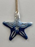 Ceramic starfish ornament in navy blue and white glaze, hanging from a natural twine cord.