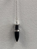 Black onyx bullet pendulum hanging from a silver chain against a textured white wall