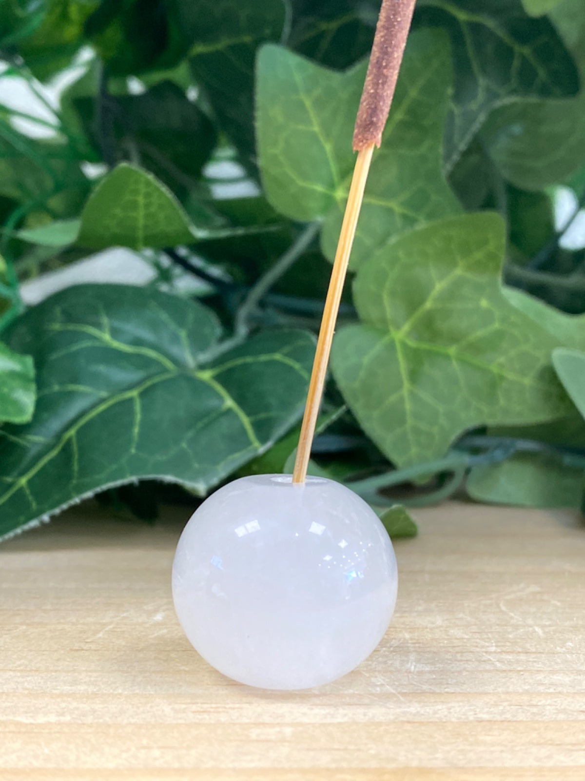 Clear quartz sphere on wooden base with wooden incense stick, green plant foliage in background