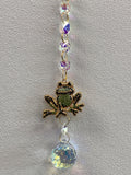 Decorative window hanger with purple faceted beads, gold-toned frog charm, and large clear crystal ball pendant
