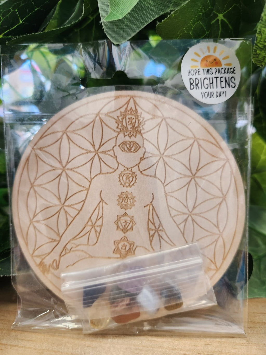 Wooden circular chakra grid with engraved flower of life pattern and seven chakra symbols, in clear packaging