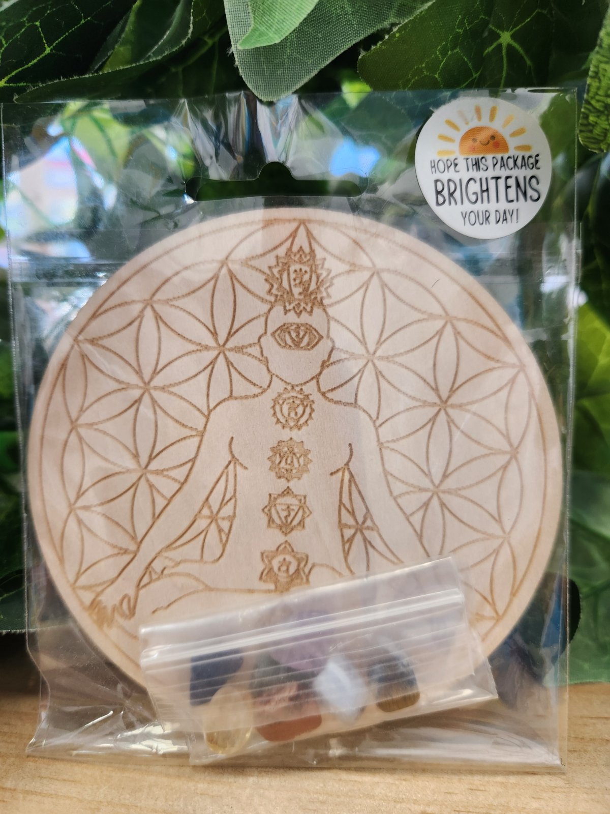 Wooden circular chakra grid with engraved flower of life pattern and seven chakra symbols, in clear packaging