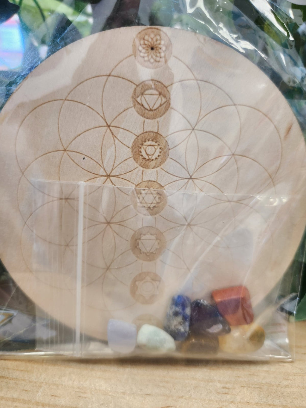 Wooden circular chakra grid with sacred geometry pattern and seven chakra symbols arranged vertically, with small raw crystals.