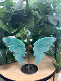 Turquoise amazonite crystal butterfly ornament with metal stand, displayed among potted plants