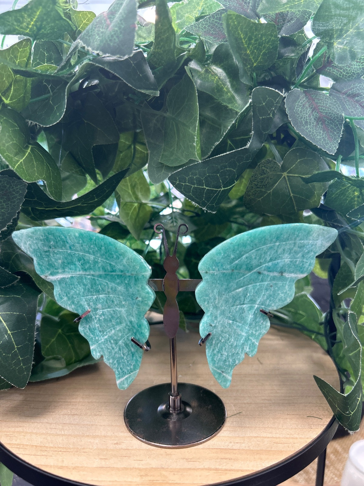 Turquoise amazonite crystal butterfly ornament with metal stand, displayed among potted plants
