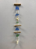 Vertical sea glass mobile with wooden beads, blue and green frosted glass pieces, a brass star, and cream ceramic charm