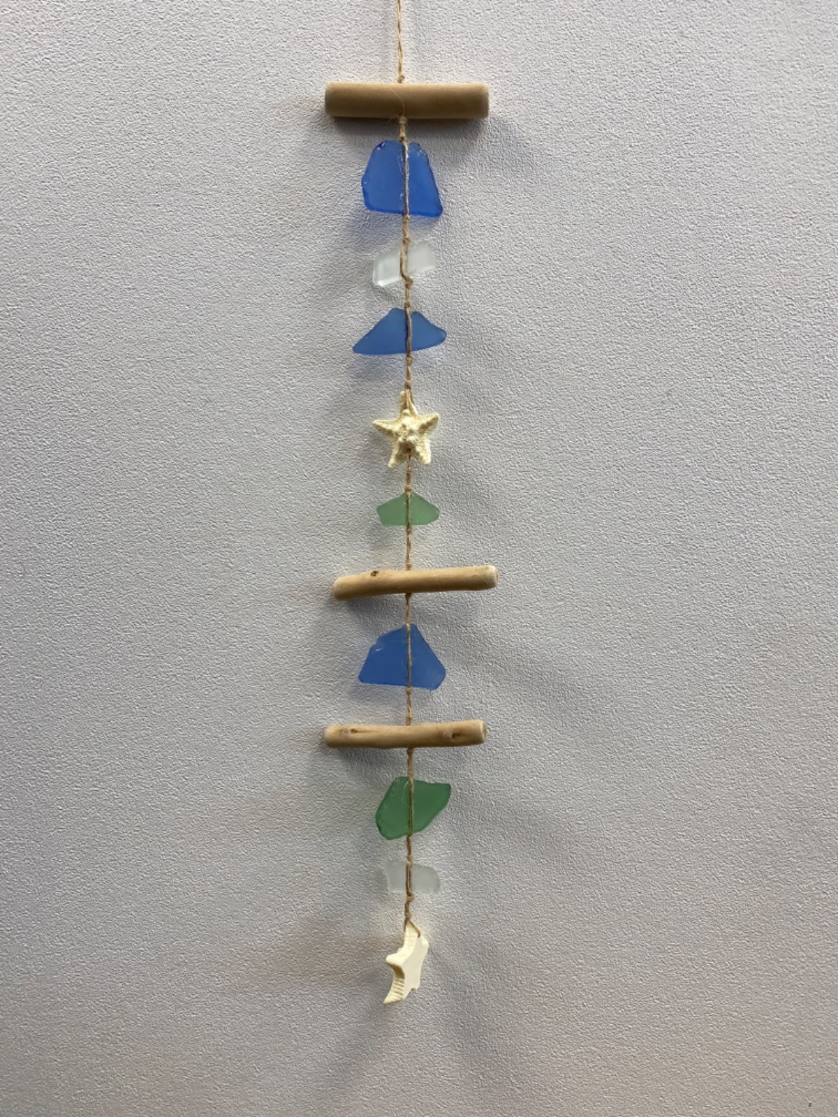 Vertical sea glass mobile with wooden beads, blue and green frosted glass pieces, a brass star, and cream ceramic charm
