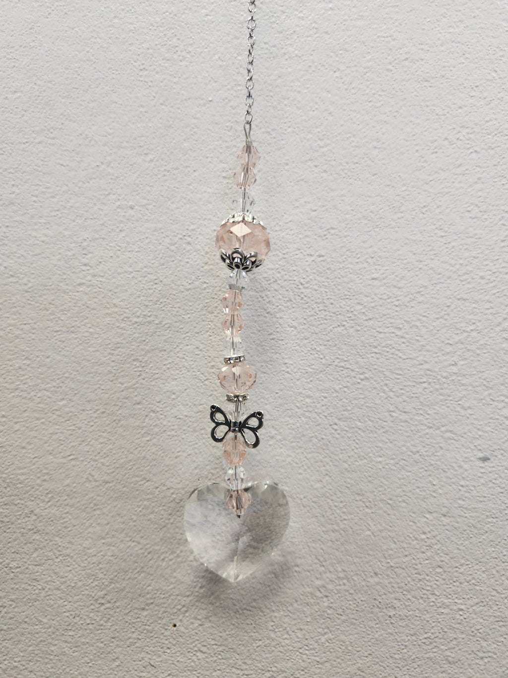 Pink beaded suncatcher with clear quartz heart charm, silver chain, and black bow accent