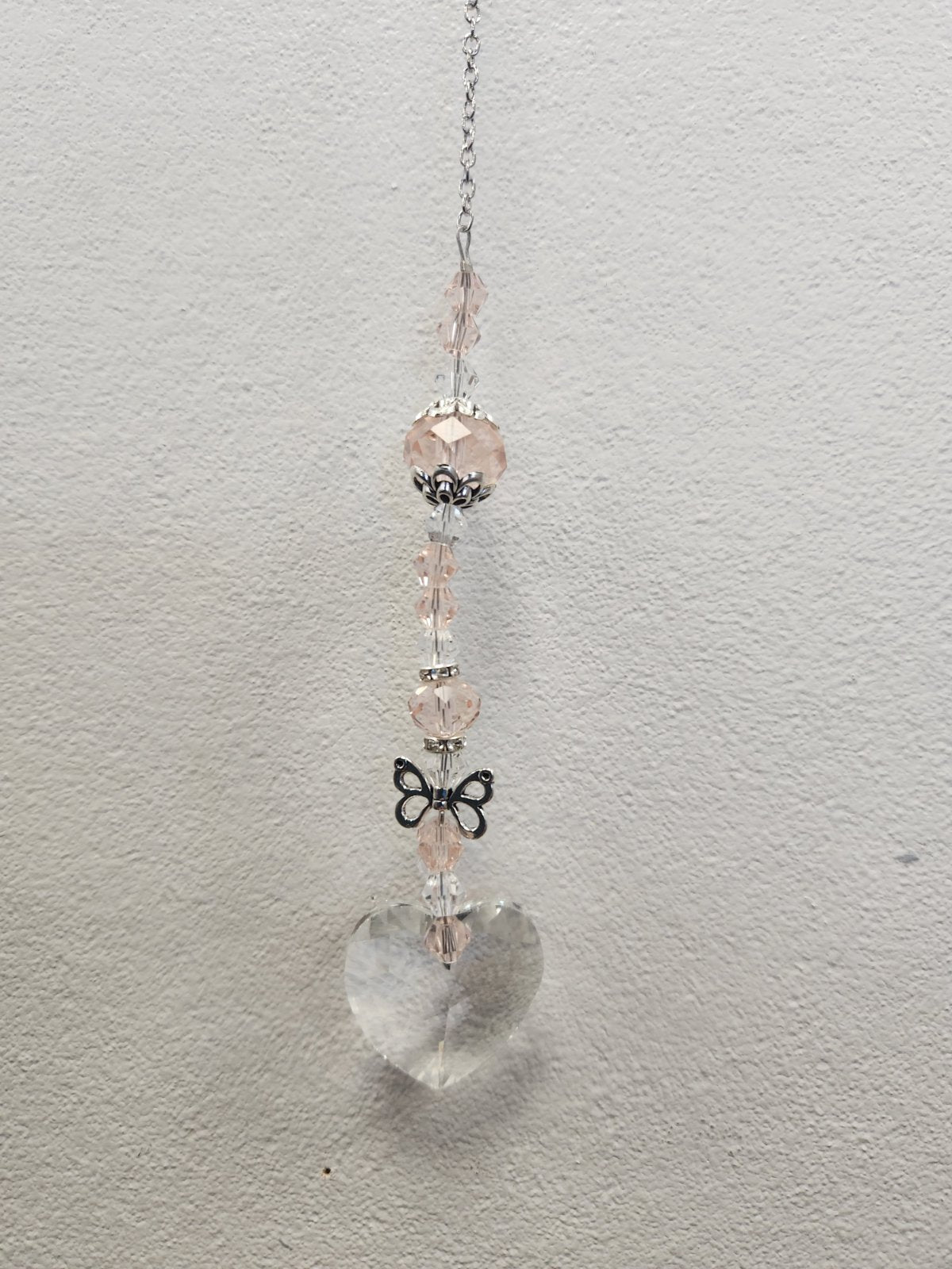 Pink beaded suncatcher with clear quartz heart charm, silver chain, and black bow accent
