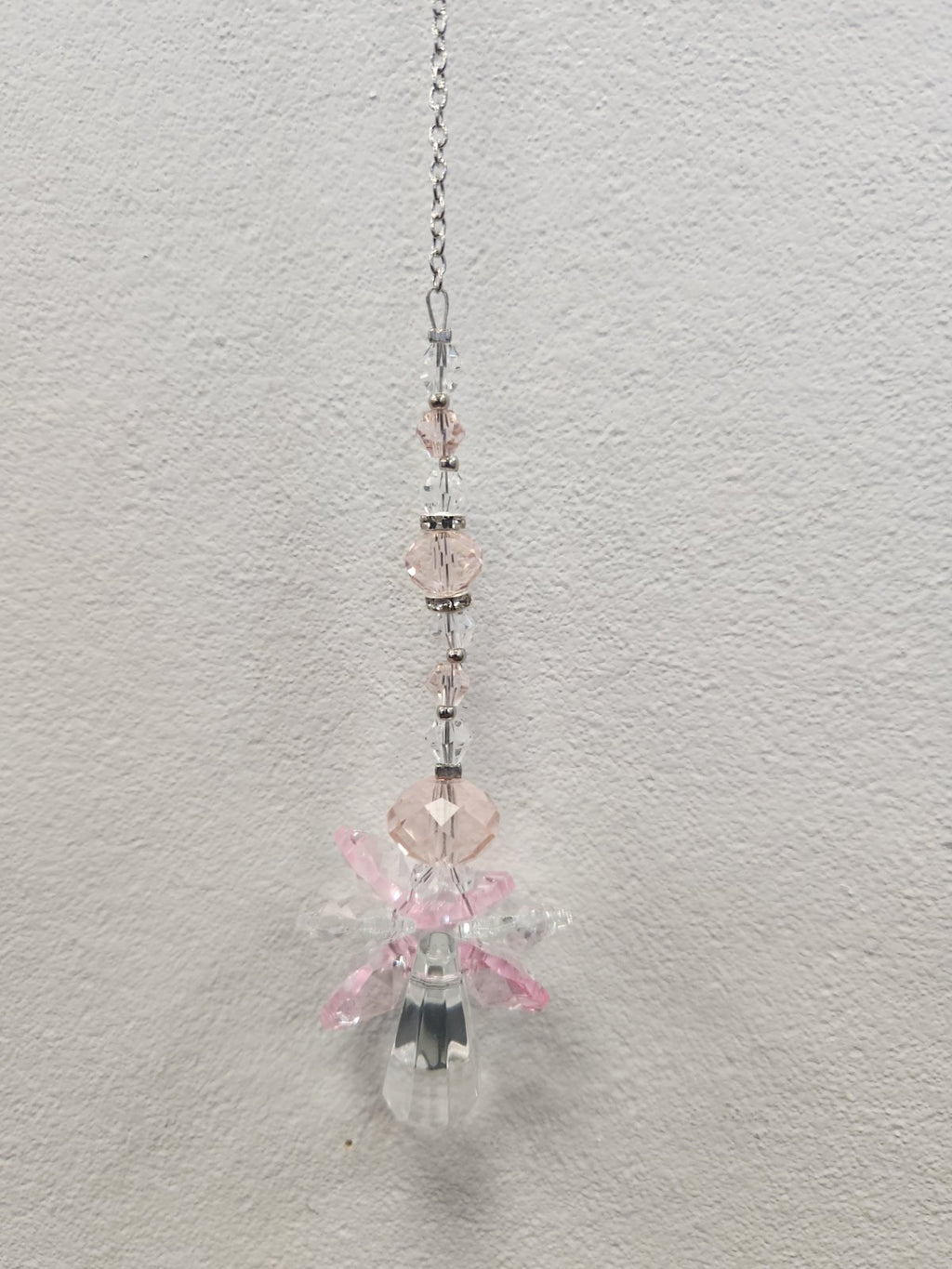 Pink beaded suncatcher with clear crystal charms hanging from a silver chain against white wall