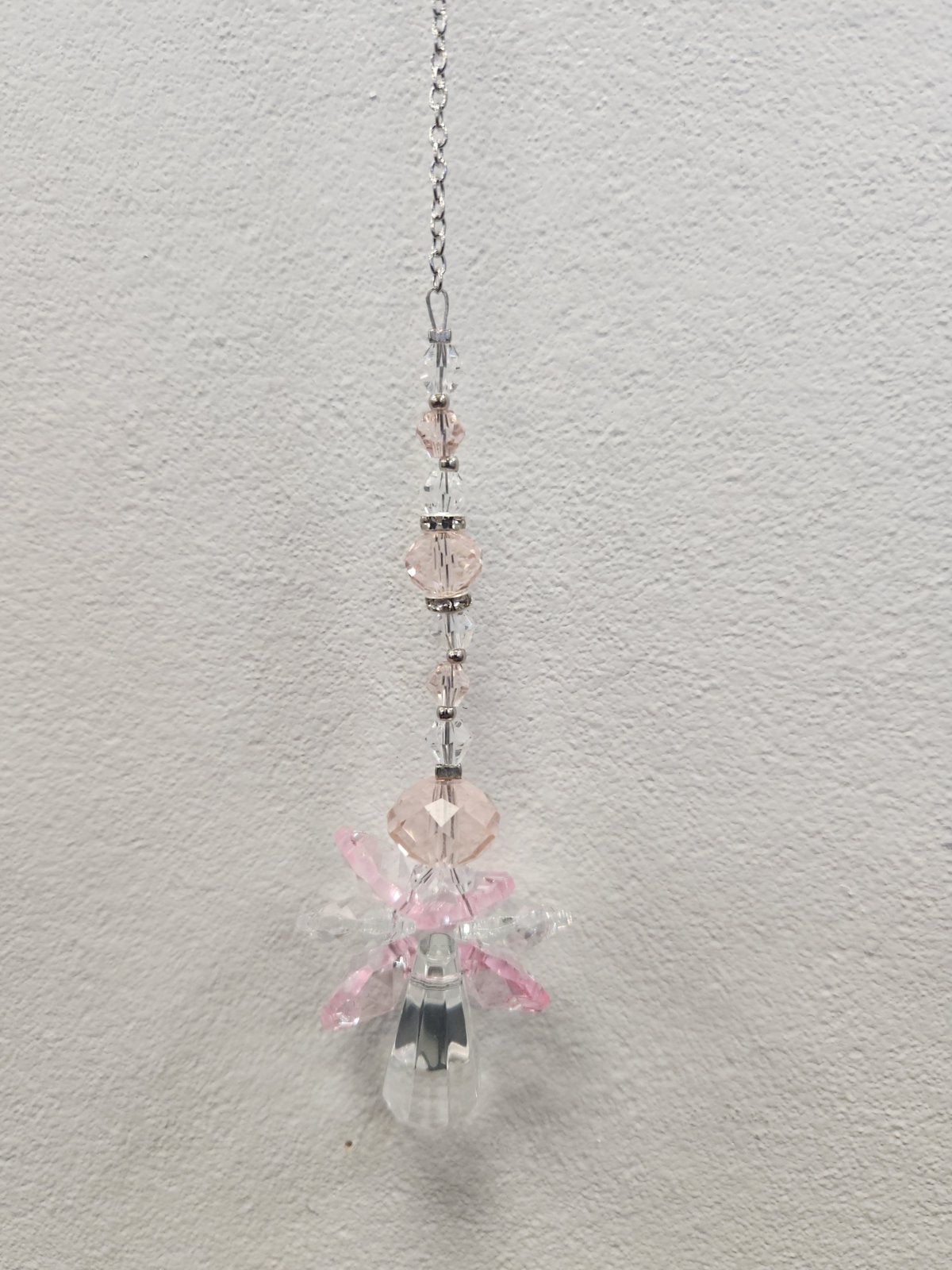 Pink beaded suncatcher with clear crystal charms hanging from a silver chain against white wall