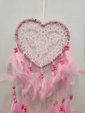 Pink and white heart-shaped dreamcatcher with lace webbing, mauve trim, and pink feathered strands with beads