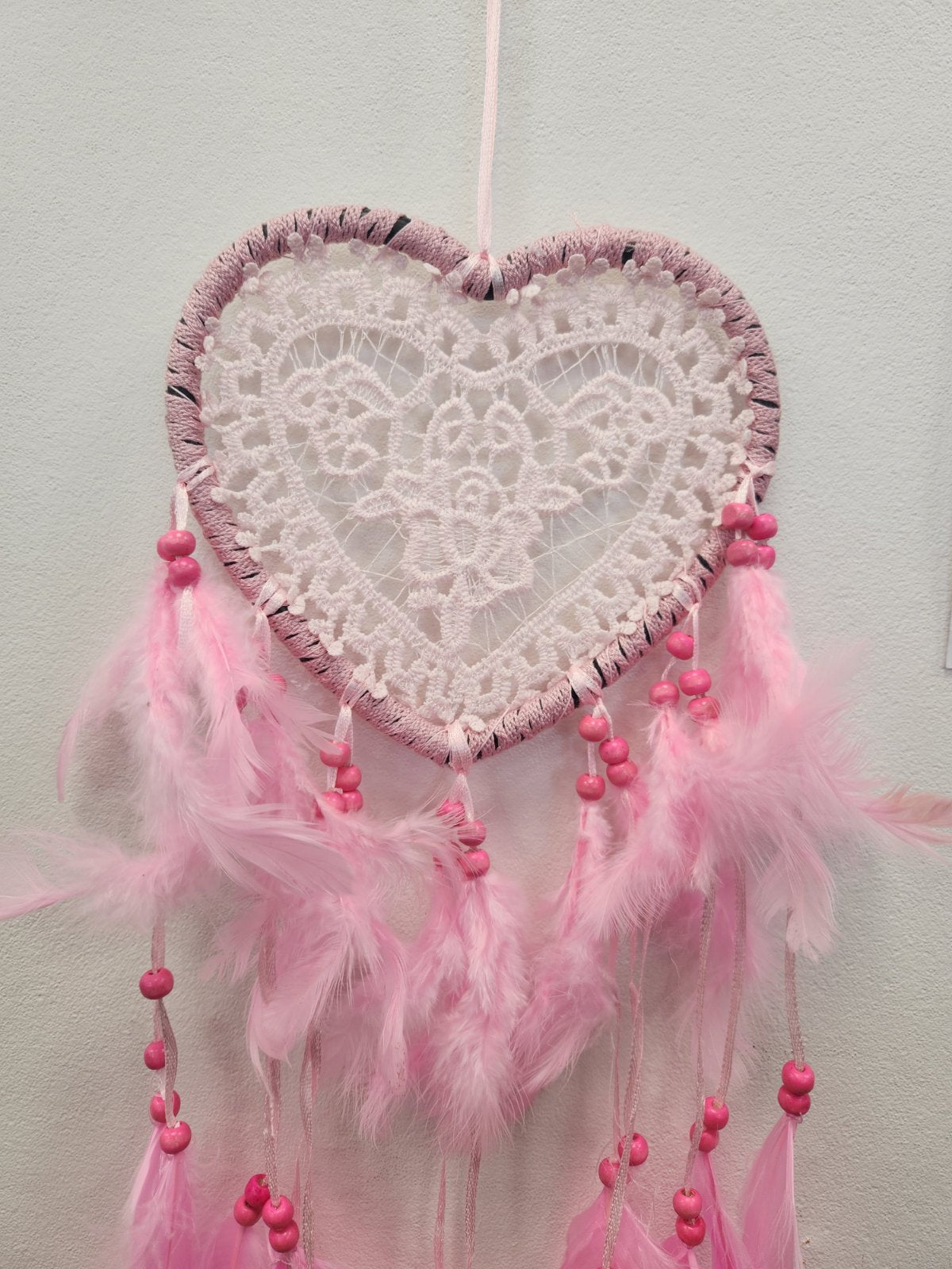 Pink and white heart-shaped dreamcatcher with lace webbing, mauve trim, and pink feathered strands with beads