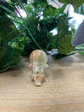 Green banded onyx angel carving, cream and tan striped, sitting on wood with potted plant behind