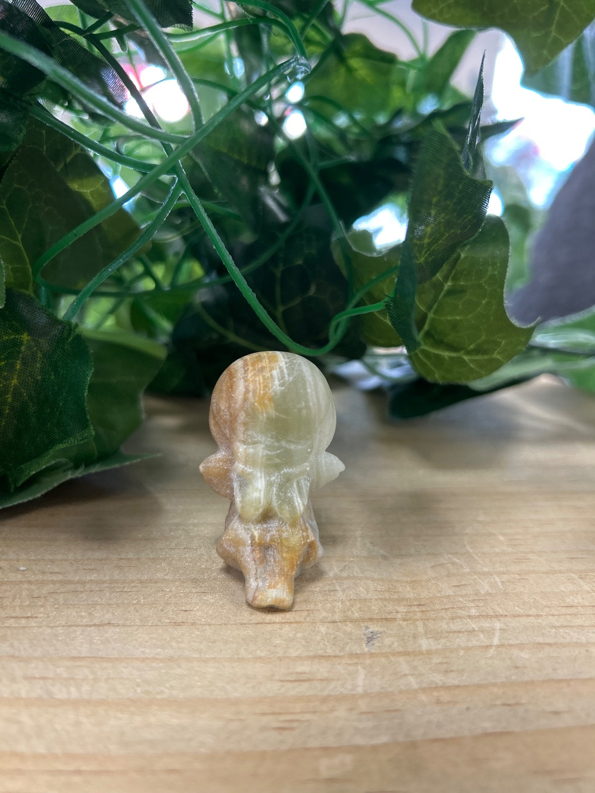Green banded onyx angel carving, cream and tan striped, sitting on wood with potted plant behind