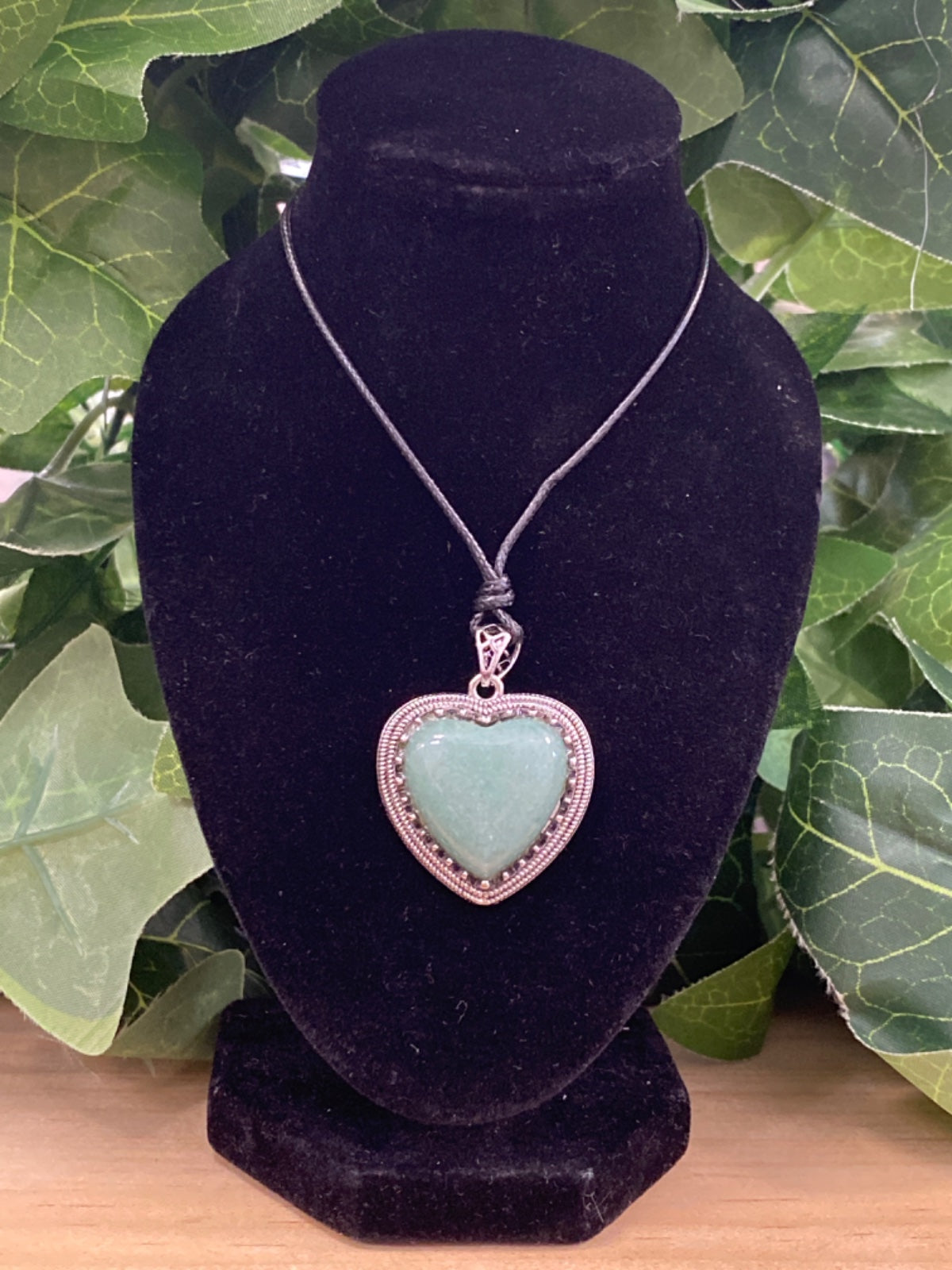 Pale green aventurine heart pendant with copper wire wrapping, hanging from grey cord on black velvet bust