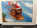Two brown kiwi birds in a golden paper boat, one wearing a red Santa hat, floating against a blue sky