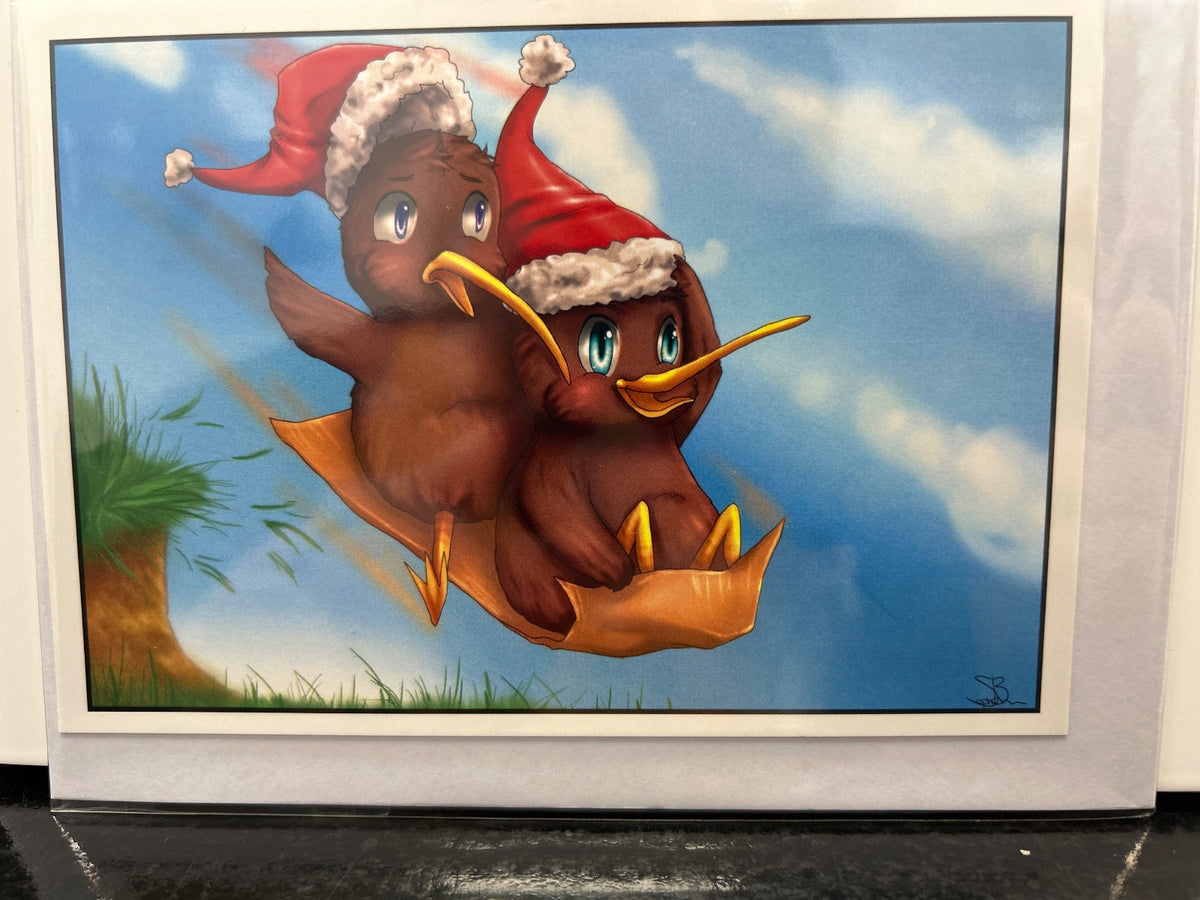 Two brown kiwi birds in a golden paper boat, one wearing a red Santa hat, floating against a blue sky