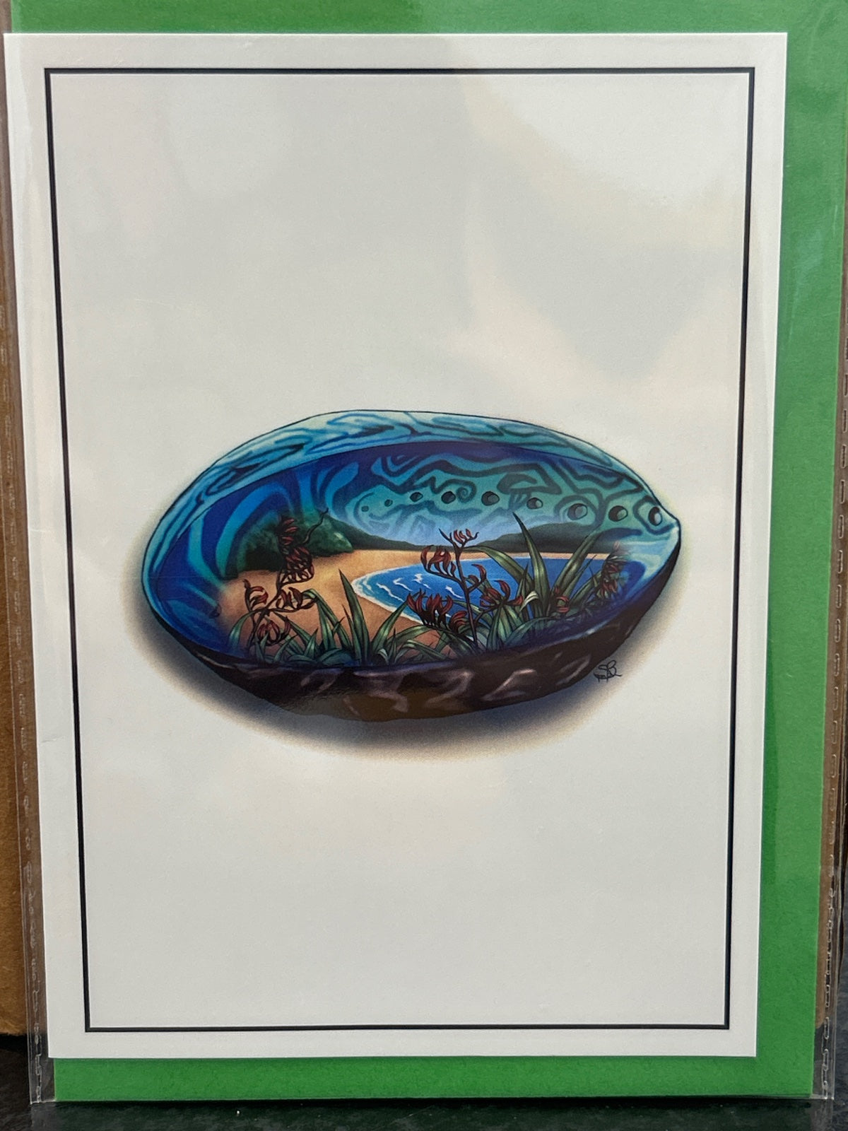 Paua shell greeting card with hand-painted landscape scene inside, blue and green tones, mounted on white card stock.